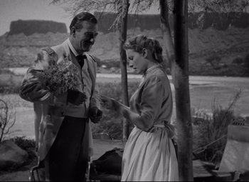 Movie still from “Rio Grande” (1950), directed by John Ford – A man and a woman standing next to each other holding flowers; Medium shot, Over the shoulder angle