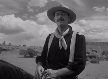 Movie still from “Rio Grande” (1950), directed by John Ford – A man in a cowboy hat on a horse in the desert; Medium shot, Low angle