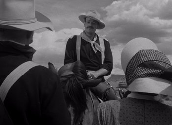 Movie still from “Rio Grande” (1950), directed by John Ford – A man sitting on top of a horse in front of a group of people; Medium shot, Low angle