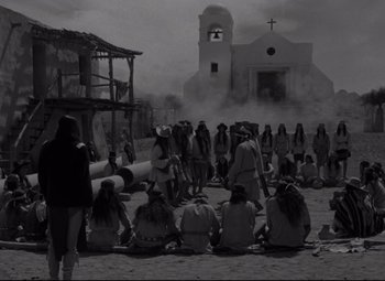 Movie still from “Rio Grande” (1950), directed by John Ford – A black and white photo of people sitting in front of a church; Wide shot, High angle
