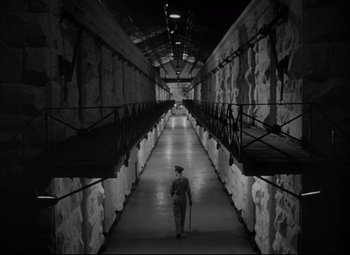 Movie still from “Riot in Cell Block 11” (1954), directed by Don Siegel – A man walking down a long hallway in a prison cell; Extreme Wide shot, High angle