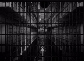 Movie still from “Riot in Cell Block 11” (1954), directed by Don Siegel – A black and white photo of a person in a jail cell; Extreme Wide shot, Low angle