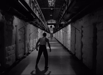 Movie still from “Riot in Cell Block 11” (1954), directed by Don Siegel – A man standing in an empty room with a baseball bat; Wide shot, Low angle