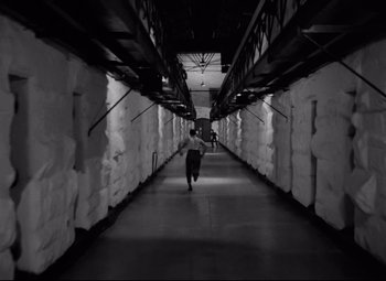 Movie still from “Riot in Cell Block 11” (1954), directed by Don Siegel – A man walking down a long hallway in a building; Extreme Wide shot, High angle