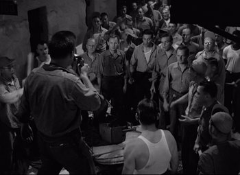 Movie still from “Riot in Cell Block 11” (1954), directed by Don Siegel – A group of men standing in a room; Wide shot, High angle