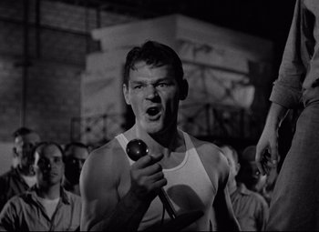 Movie still from “Riot in Cell Block 11” (1954), directed by Don Siegel – A black and white photo of a man holding a microphone; Medium shot, Low angle