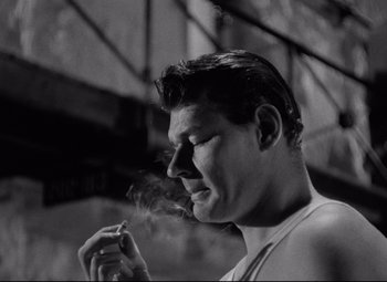 Movie still from “Riot in Cell Block 11” (1954), directed by Don Siegel – A black and white photo of a man smoking a cigarette; Close Up shot, Low angle