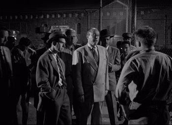 Movie still from “Riot in Cell Block 11” (1954), directed by Don Siegel – A black and white photo of a group of men in suits and hats; Medium shot, Low angle