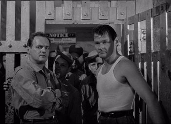 Movie still from “Riot in Cell Block 11” (1954), directed by Don Siegel – A black - and - white photo of two men and a woman; Medium shot, Low angle