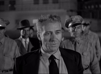 Movie still from “Riot in Cell Block 11” (1954), directed by Don Siegel – Black and white photograph of a man in a suit and tie; Medium shot, Low angle
