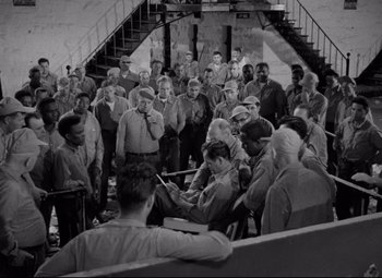 Movie still from “Riot in Cell Block 11” (1954), directed by Don Siegel – A group of people standing around a building; Wide shot, High angle