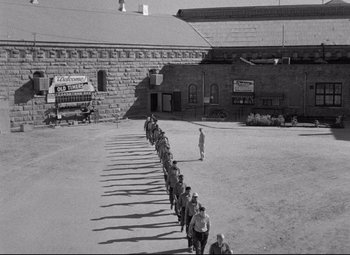 Movie still from “Riot in Cell Block 11” (1954), directed by Don Siegel – A black - and - white photo of a long line of people; Extreme Wide shot, High angle