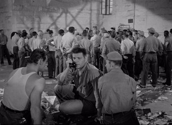 Movie still from “Riot in Cell Block 11” (1954), directed by Don Siegel – A black and white photo of a group of men; Wide shot, High angle