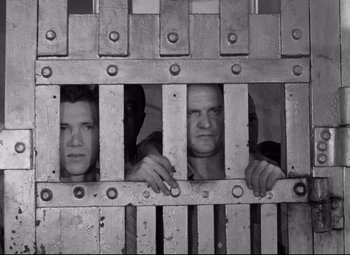 Movie still from “Riot in Cell Block 11” (1954), directed by Don Siegel – Two men looking through the bars of a jail cell; Medium shot, Low angle