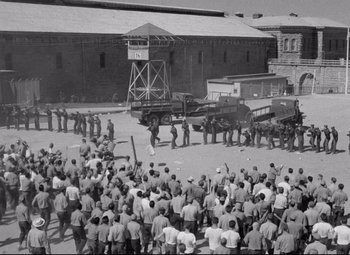 Movie still from “Riot in Cell Block 11” (1954), directed by Don Siegel – A group of men standing next to each other in front of a truck; Extreme Wide shot, High angle