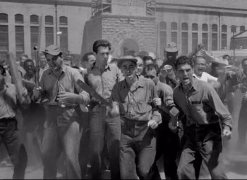 Movie still from “Riot in Cell Block 11” (1954), directed by Don Siegel – A group of men are marching down a street; Wide shot, High angle