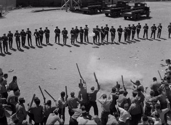 Movie still from “Riot in Cell Block 11” (1954), directed by Don Siegel – A group of men standing next to each other on top of a dirt field; Extreme Wide shot, High angle
