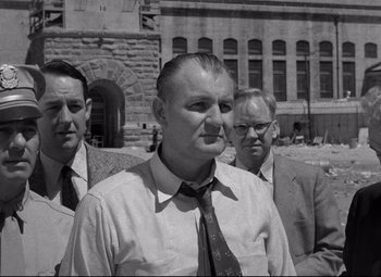 Movie still from “Riot in Cell Block 11” (1954), directed by Don Siegel – A black - and - white photo of three men standing next to each other in front of a building; Medium shot, Over the shoulder angle