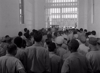 Movie still from “Riot in Cell Block 11” (1954), directed by Don Siegel – Black and white photograph of a group of people in a prison cell; Wide shot, High angle