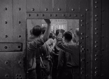 Movie still from “Riot in Cell Block 11” (1954), directed by Don Siegel – Black and white photograph of a group of people standing in front of a door; Wide shot, High angle