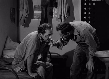 Movie still from “Riot in Cell Block 11” (1954), directed by Don Siegel – Two men are sitting and one of them is holding something in his mouth; Medium shot, High angle