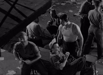 Movie still from “Riot in Cell Block 11” (1954), directed by Don Siegel – A black and white photo of a group of men sitting around; Wide shot, High angle