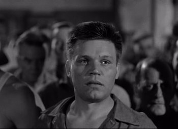 Movie still from “Riot in Cell Block 11” (1954), directed by Don Siegel – A black - and - white photo of a man in front of a group of people; Close Up shot, Low angle