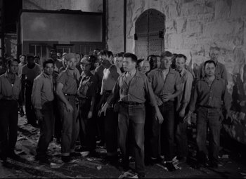 Movie still from “Riot in Cell Block 11” (1954), directed by Don Siegel – Black and white photograph of a group of men standing in front of a building; Wide shot, High angle