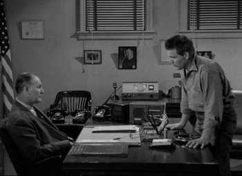 Movie still from “Riot in Cell Block 11” (1954), directed by Don Siegel – A man and a woman sitting at a desk; Medium shot, Over the shoulder angle