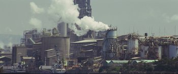 Movie still from “Ritual” (2000), directed by Hideaki Anno – Smoke billows out of a large industrial plant; Extreme Wide shot, Low angle