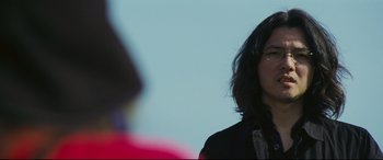 Movie still from “Ritual” (2000), directed by Hideaki Anno – A woman wearing a black shirt and a tie; Close Up shot, Over the shoulder angle