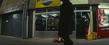 Movie still from “Ritual” (2000), directed by Hideaki Anno – A person walking down the street in front of a store; Wide shot, Low angle