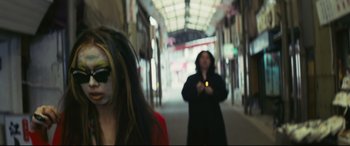 Movie still from “Ritual” (2000), directed by Hideaki Anno – A woman is walking down the street with a cell phone in her hand; Close Up shot, Over the shoulder angle