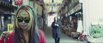 Movie still from “Ritual” (2000), directed by Hideaki Anno – A woman walking down a street with a bunch of other people; Close Up shot, Over the shoulder angle