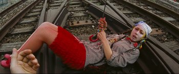 Movie still from “Ritual” (2000), directed by Hideaki Anno – A woman laying on a train track holding onto a leash; Medium shot, Overhead angle