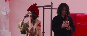 Movie still from “Ritual” (2000), directed by Hideaki Anno – A woman in a red hat is holding a pipe in front of a man; Medium shot, Low angle