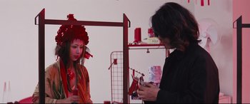 Movie still from “Ritual” (2000), directed by Hideaki Anno – A woman wearing a red hat and holding a cell phone; Medium shot, Over the shoulder angle
