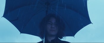 Movie still from “Ritual” (2000), directed by Hideaki Anno – A man holding an open umbrella in the rain; Close Up shot, Low angle