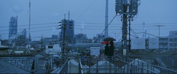 Movie still from “Ritual” (2000), directed by Hideaki Anno – A person holding an umbrella while standing on top of a building; Extreme Wide shot, Low angle