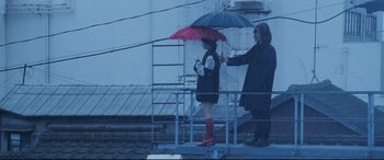 Movie still from “Ritual” (2000), directed by Hideaki Anno – A woman holding an umbrella while standing next to another woman; Wide shot, Low angle