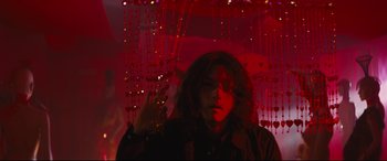 Movie still from “Ritual” (2000), directed by Hideaki Anno – A woman standing in front of a red curtain; Medium shot, Low angle