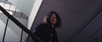 Movie still from “Ritual” (2000), directed by Hideaki Anno – A man standing on a staircase wearing a black shirt; Medium shot, Low angle