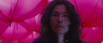 Movie still from “Ritual” (2000), directed by Hideaki Anno – A man with long hair wearing glasses and holding an umbrella; Close Up shot, Low angle