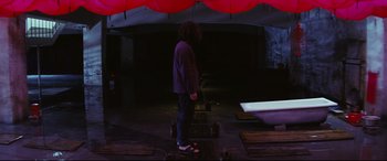 Movie still from “Ritual” (2000), directed by Hideaki Anno – A person standing in a dark room under an umbrella; Wide shot, High angle
