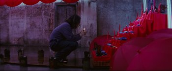 Movie still from “Ritual” (2000), directed by Hideaki Anno – A woman lighting a cigarette in front of a bunch of candles; Wide shot, High angle