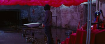 Movie still from “Ritual” (2000), directed by Hideaki Anno – A person standing in a room under an awning; Wide shot, High angle