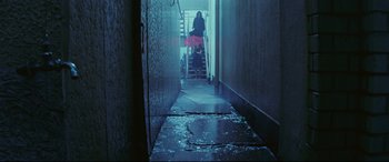 Movie still from “Ritual” (2000), directed by Hideaki Anno – A woman in a pink skirt walking down the stairs of a building; Wide shot, High angle