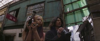 Movie still from “Ritual” (2000), directed by Hideaki Anno – A man and a woman are holding a camera; Medium shot, Low angle