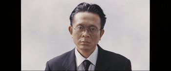 Movie still from “Ritual” (2000), directed by Hideaki Anno – A man in a suit and tie wearing glasses; Close Up shot, Low angle