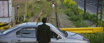 Movie still from “Ritual” (2000), directed by Hideaki Anno – A man standing next to a car on the side of a train track; Extreme Wide shot, High angle